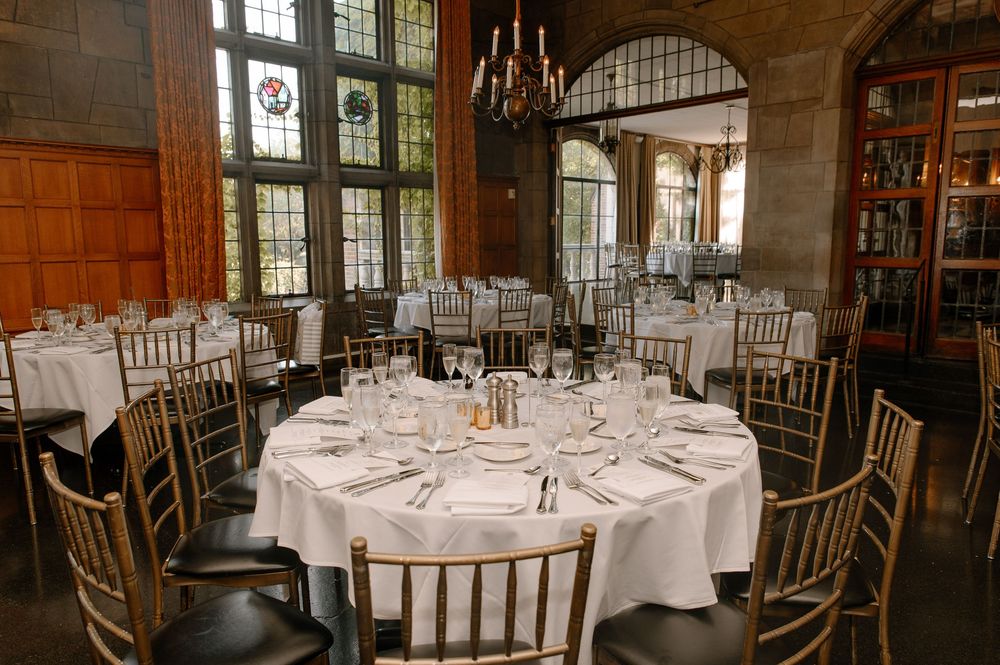 Elegant wedding reception tables with white linens and chiavari chairs set in a rustic wooden event venue.