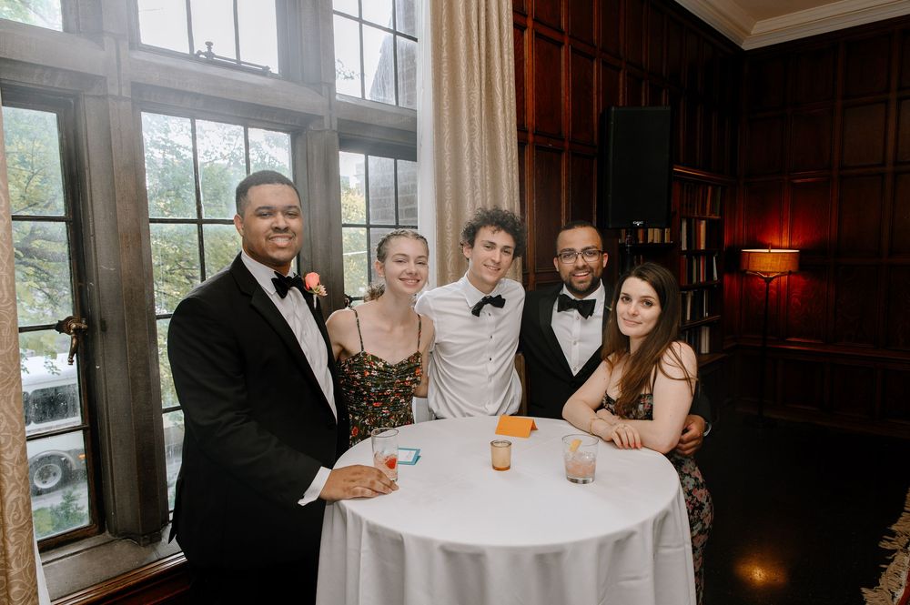 Wedding guests gather around a table during a reception celebration with drinks and smiles.