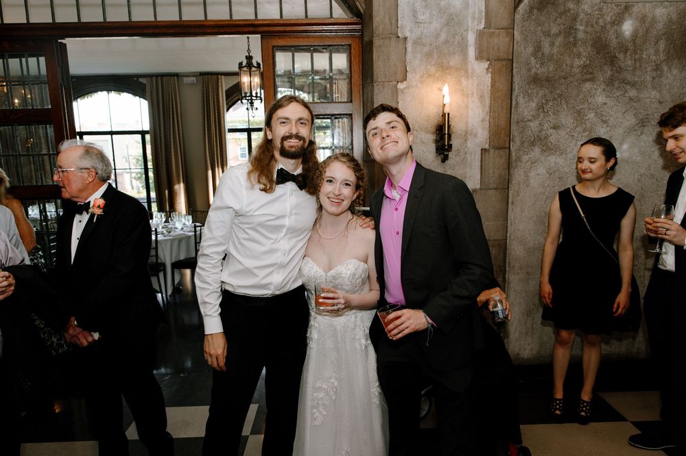 A festive wedding reception scene with guests mingling in a grand historic building interior.