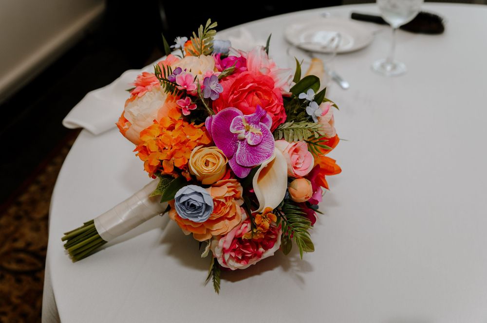 Vibrant coral and pink wedding bouquets displayed on a white tablecloth at a reception venue.
