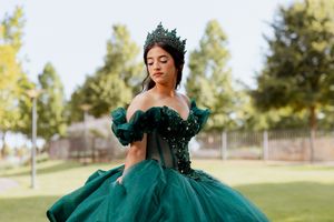 Stunning emerald quinceanera gown with beaded bodice sparkles in an outdoor garden setting.