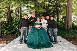 Wedding party in emerald green dresses poses outdoors under trees for formal group photos.