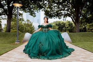 Emerald green ballgown with intricate beading flows gracefully across a garden pathway in sunlight.