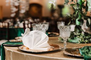 Elegant wedding reception table setting with crystal glassware, white napkins, and emerald green accents.