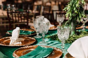 Elegant table settings with emerald green accents and crystal glassware at wedding reception.
