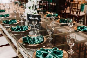 Formal dining table decorated with crystal glasses, emerald green charger plates, and natural greenery garland.
