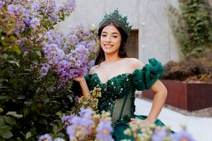 Woman in off-shoulder green gown stands gracefully beside blooming lavender flowers.