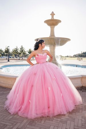 Stunning pink ball gown with voluminous tulle skirt photographed in front of an elegant stone fountain.