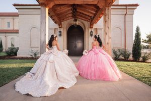 Two quinceanera dresses in white and pink displayed on the exterior steps of an elegant Spanish colonial church.