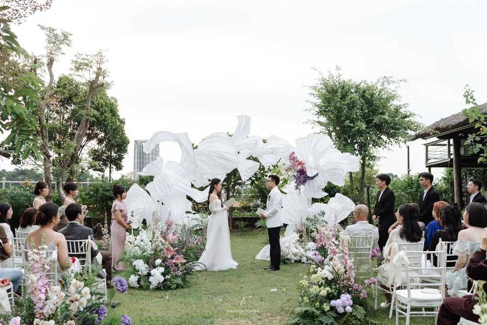 Couple at altar during outdoor garden wedding with white floral arch decorations.