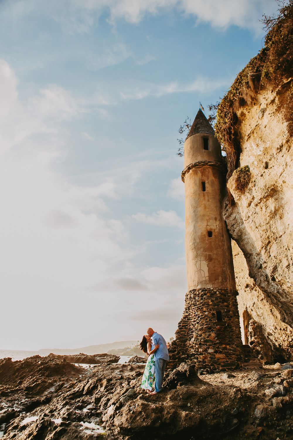Lighthouse tower in Laguna Beach engagement photos with couple kissing on rocks.