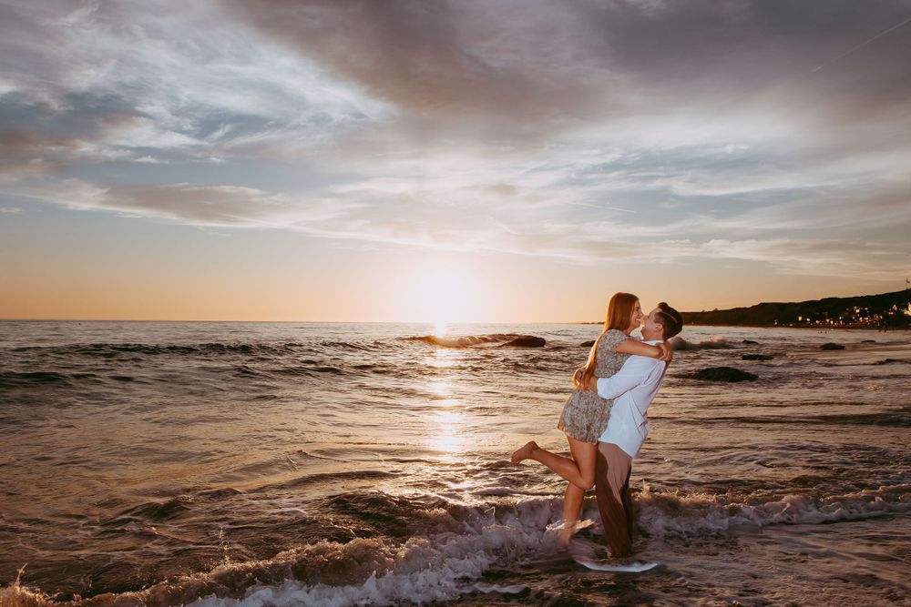 A Laguna beach at sunset with warm golden light reflecting off gentle ocean waves and misty clouds in the sky.