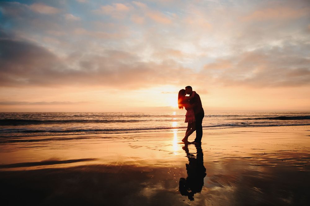 Wedding Couple kissing on a sunset beach with orange and pink sky reflecting on the wet sand in Laguna Beach.
