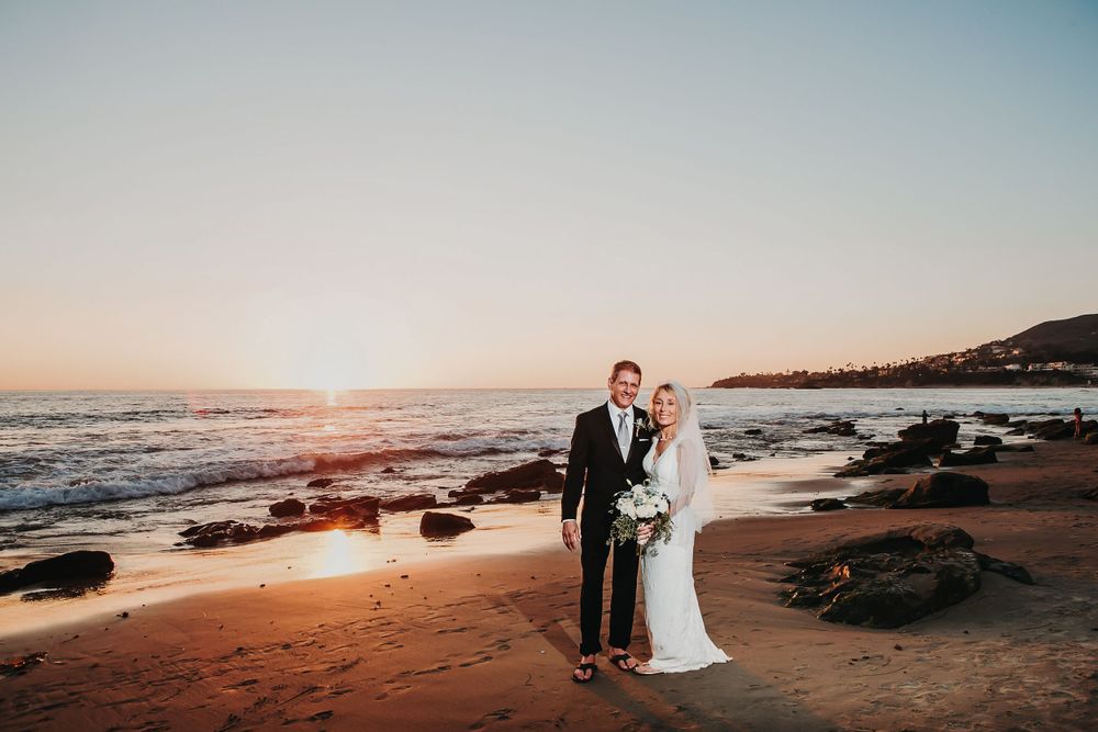 Laguna Beach sunset beach wedding ceremony with rocky coastline and warm glowing sky in the background.