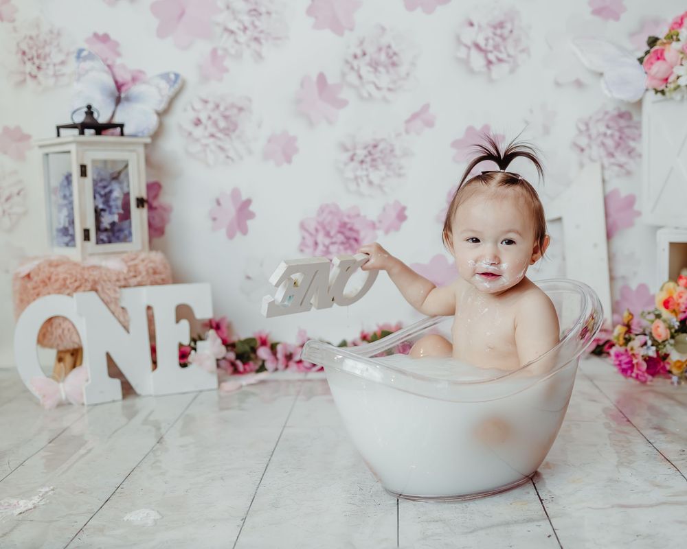 Professional baby photography with white bathtub prop against floral wallpaper in delicate pink tones.