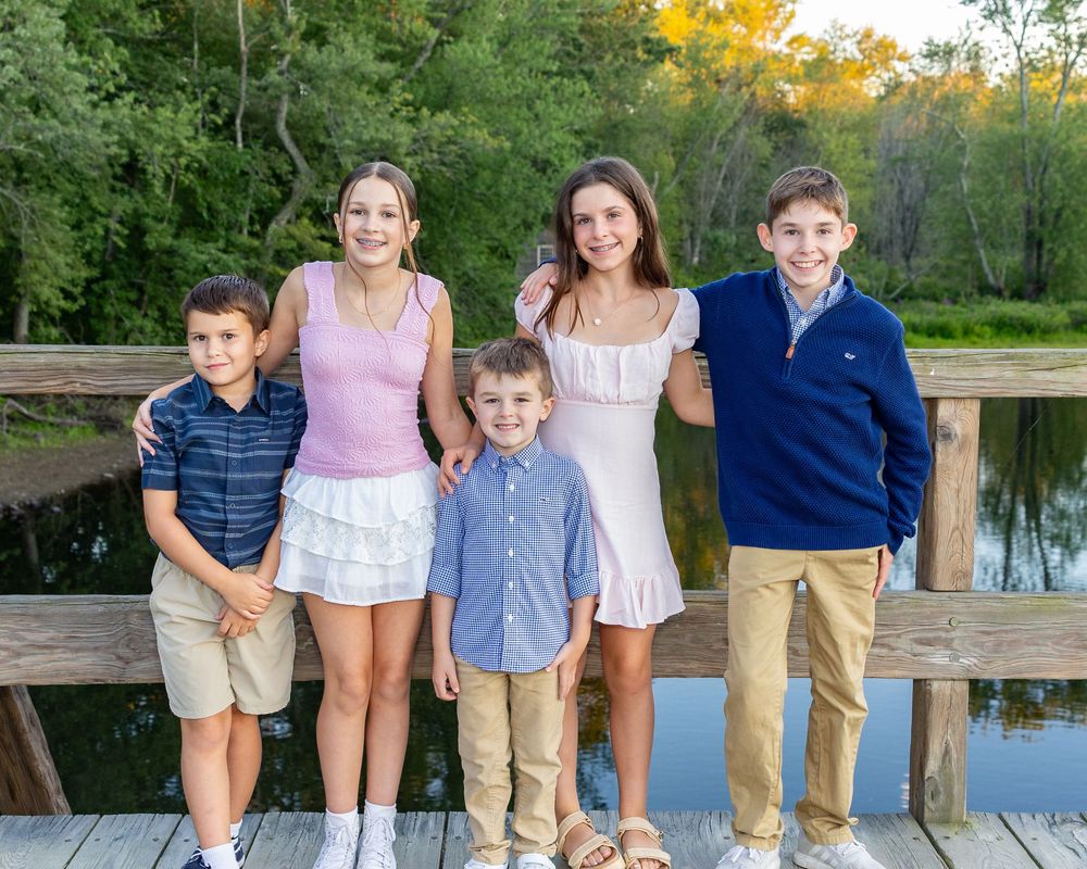 Cousins in coordinated blue and white outfits pose together on wooden North Bridge in Concord, MA during extended family photos in Fall.