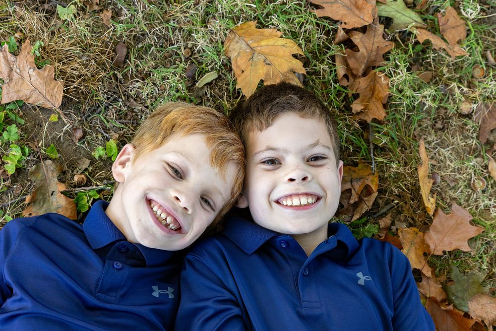 Brothers smile in an fall setting with colorful leaves at a photo session at Old North Bridge in Concord, MA with Lisa West Photography