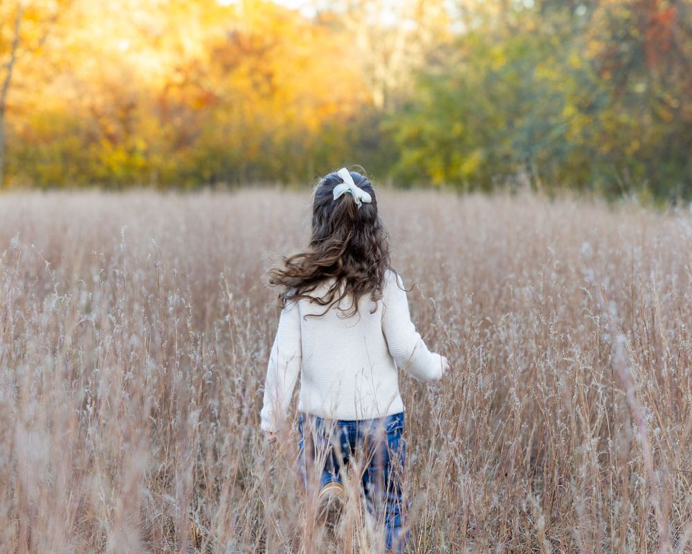 A young girl frolics in a grassy field during a family photo session Wolbach Farm in Sudbury, MA with Lisa West Photography.