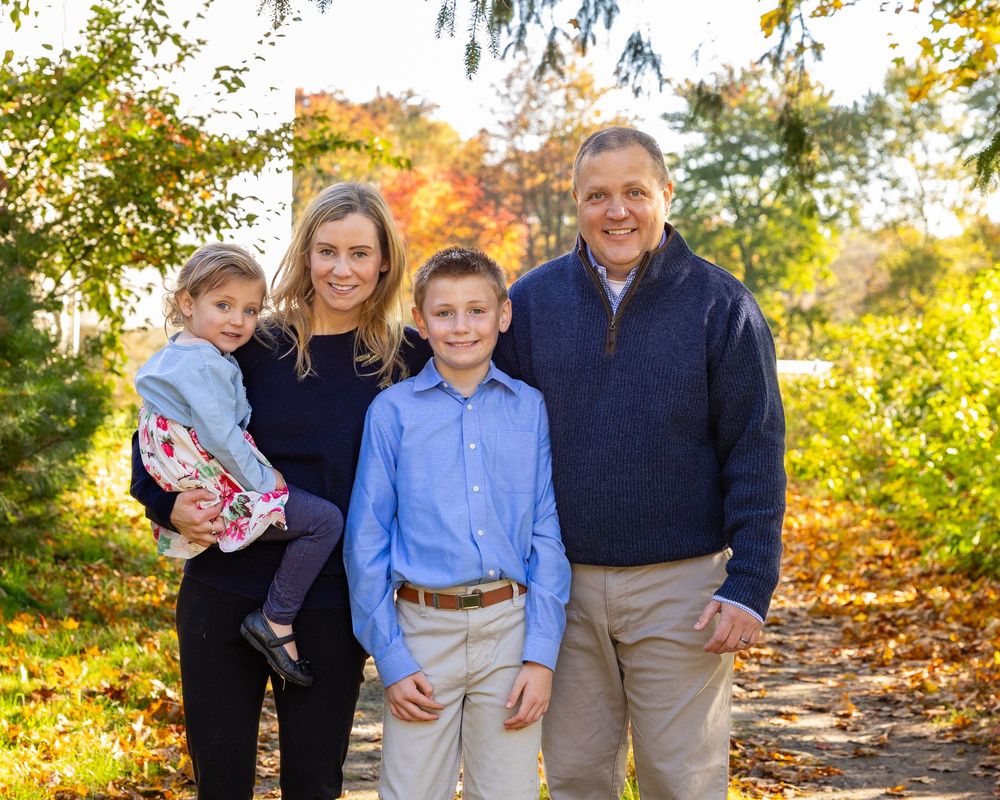 A family poses for a fall portrait with bright leaves during family photo session at Wolbach Farm in Sudbury, MA with Lisa West Photography.