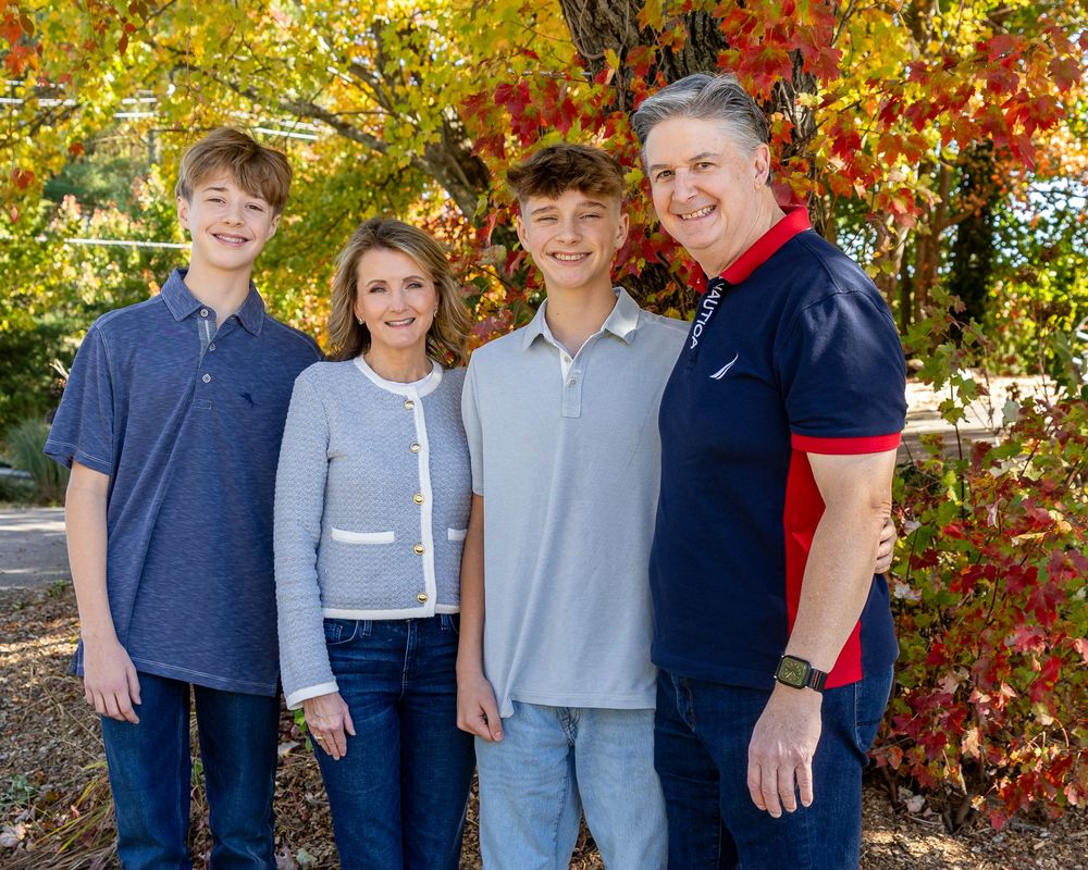A family poses in an fall setting with colorful leaves at a photo session at Mistletoe Christmas Tree Farm in Stow, MA with Lisa West Photos