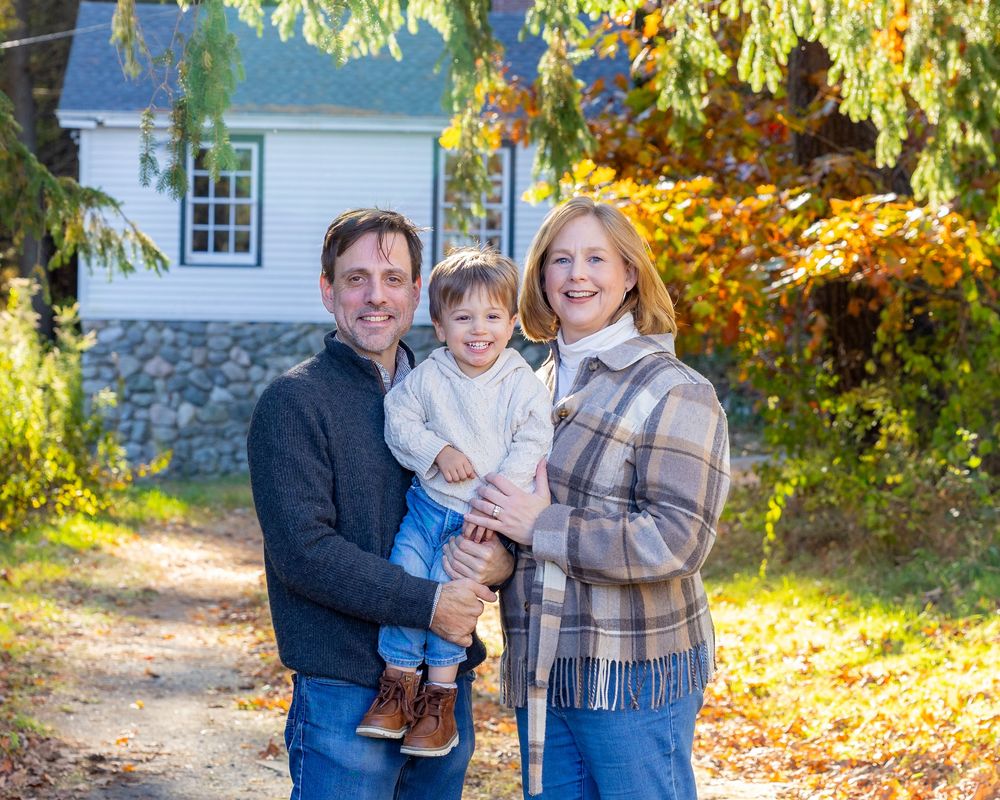 A family poses for a fall portrait with bright leaves during family photo session at Wolbach Farm in Sudbury, MA with Lisa West Photography.