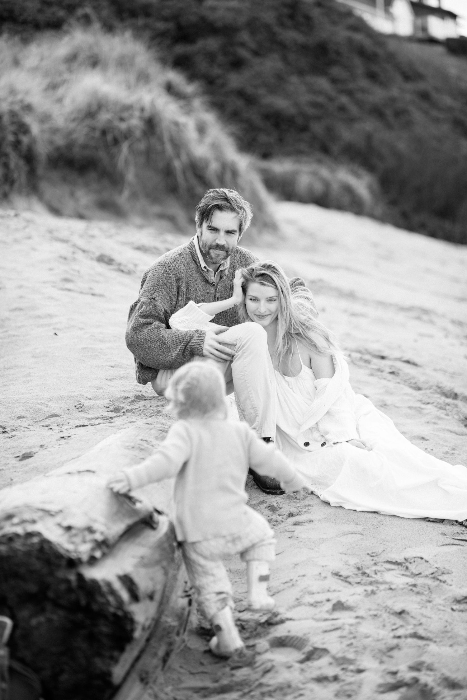 A romantic black and white photo series of a couple sitting together at the beach.
