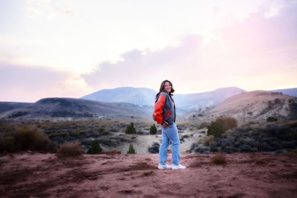 A hiker wearing a backpack explores scenic red rock terrain during sunset in a desert landscape.
