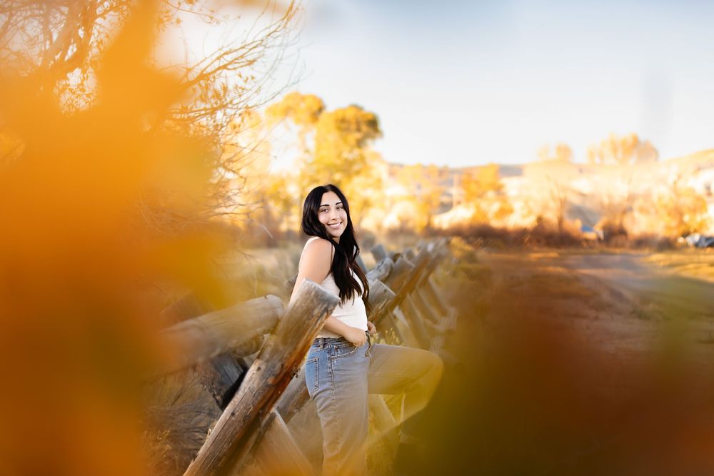 Young figure in white dress poses joyfully against a vibrant sunset backdrop in a field at golden hour.