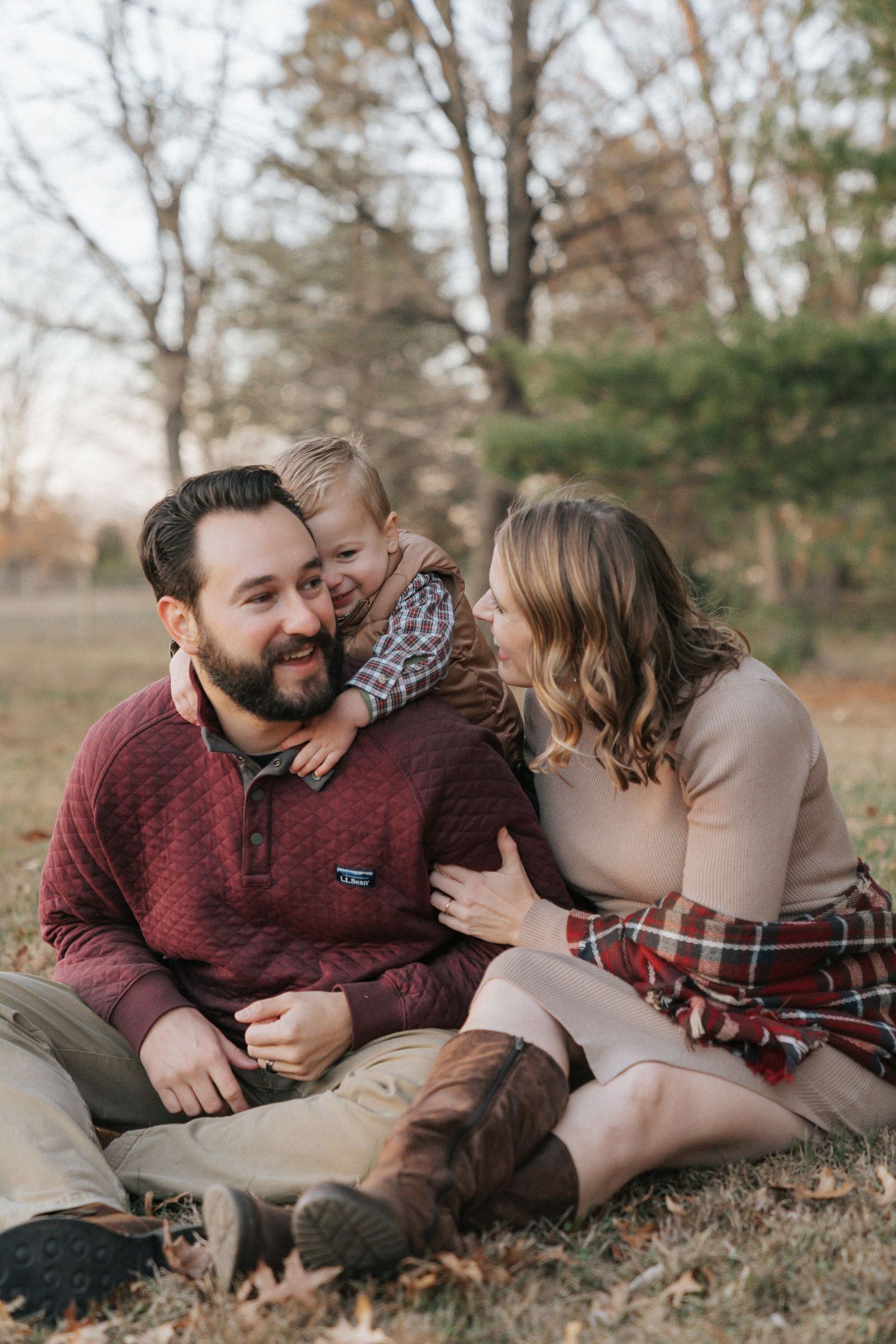 A family shares a tender moment together while sitting on autumn grass in an outdoor setting.