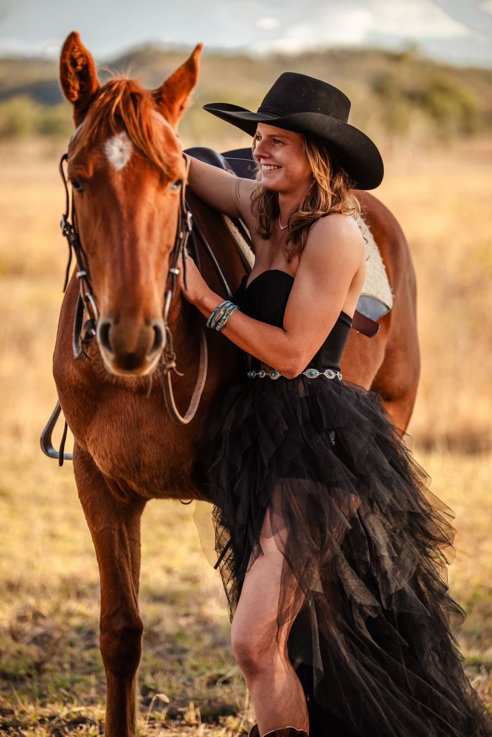 Person in black tulle dress sharing tender moment with russet horse in golden sunlit field during sunset.