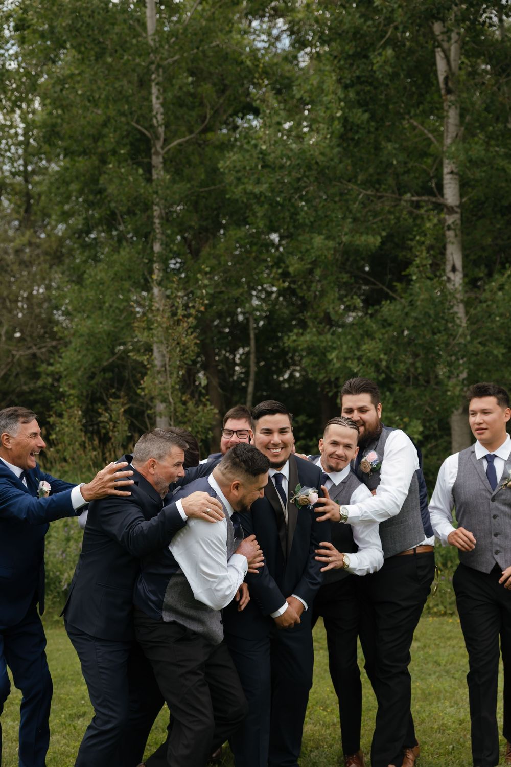 A fun sequence of groomsmen forming a line and falling over like dominoes in an outdoor setting with trees.