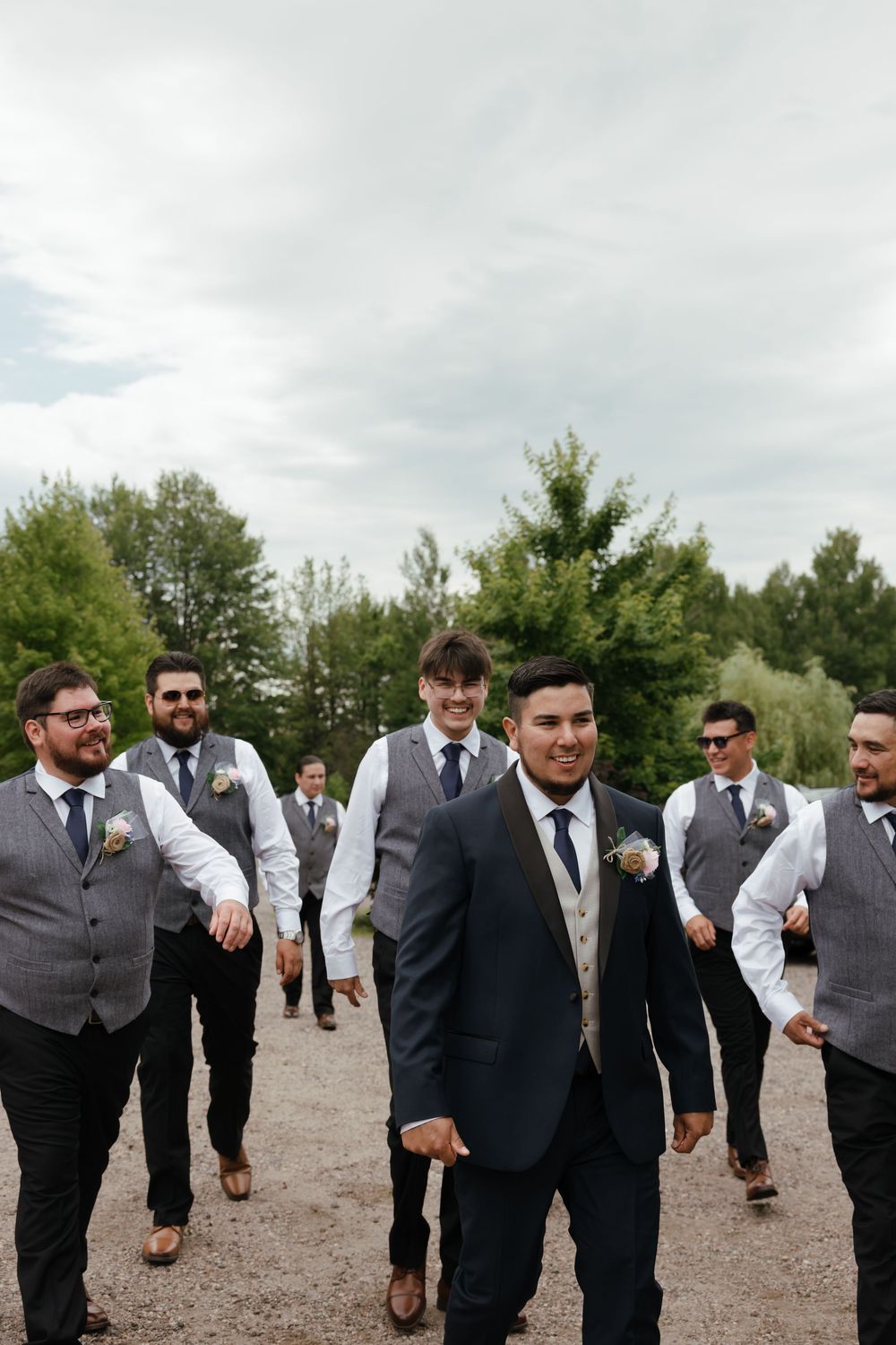 Groomsmen strolling together on gravel path in coordinated grey and black wedding attire.