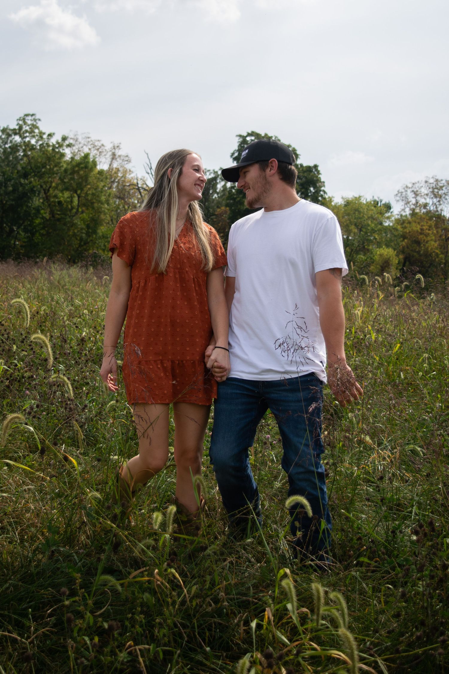 Couple walking together through tall grass, smiling at each other