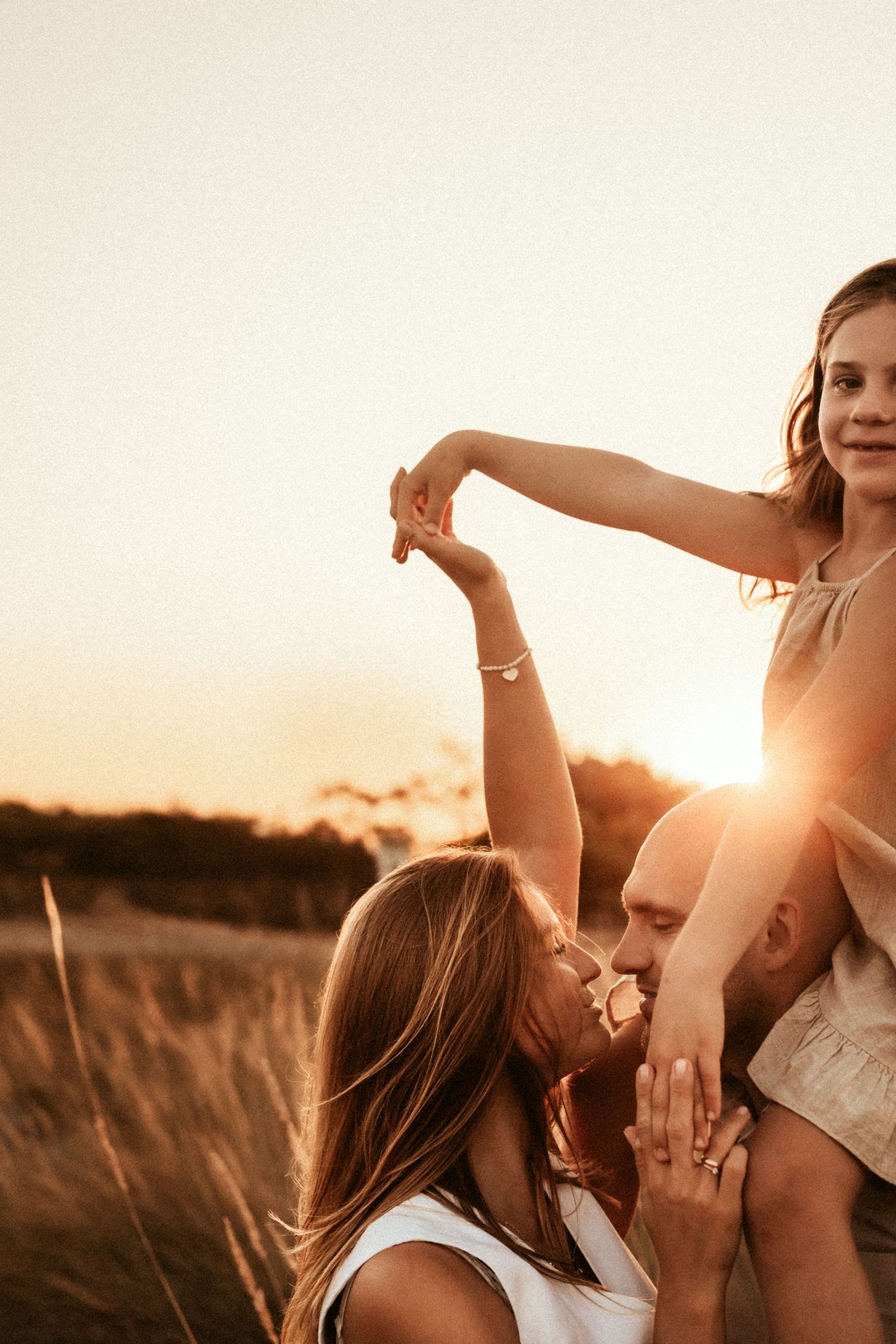 A couple shares an intimate moment together at sunset in a field of tall grass with their family. Javea photographer
