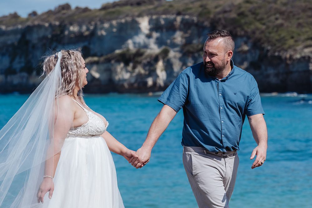 Couple in wedding attire walk and pose together along beautiful turquoise Mediterranean coastline.