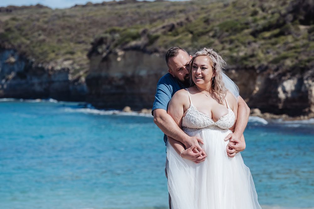 Romantic seaside couple shoot on a rocky beach with bright turquoise waters in the background.