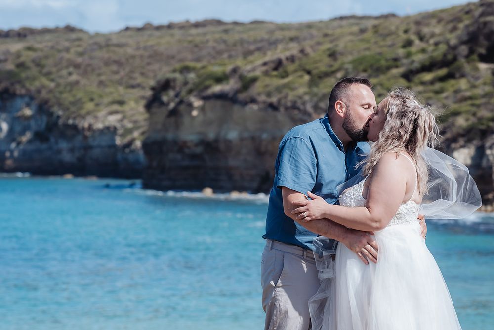 Couple sharing intimate moments during their beach wedding photoshoot with ocean waves and cliffs in the background.