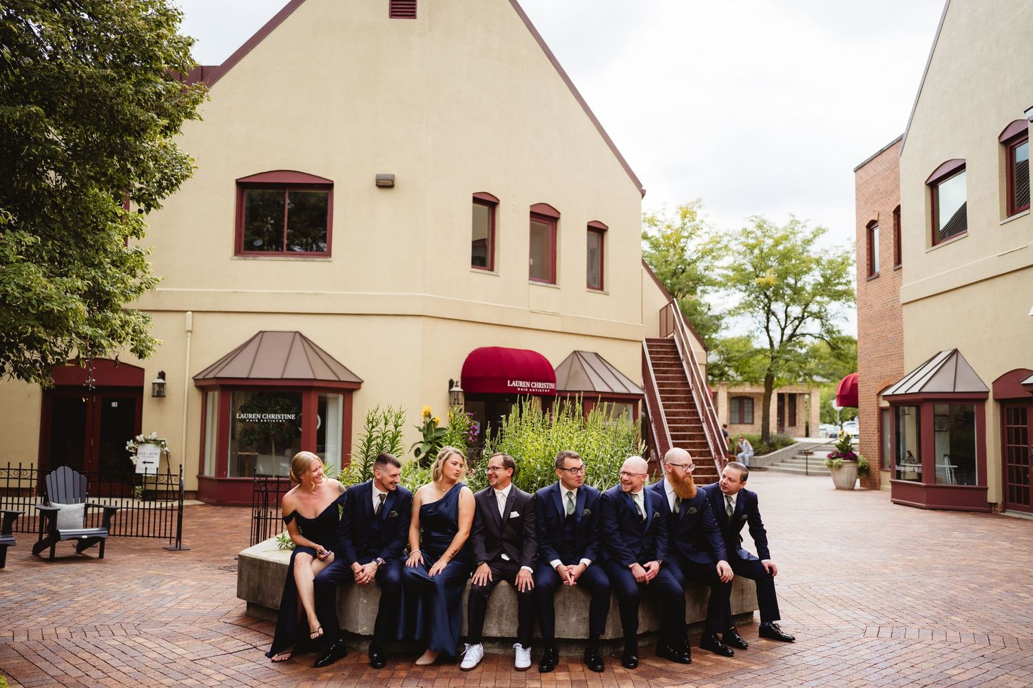 Lineup of formally dressed wedding party members standing against exterior brick wall of event venue.