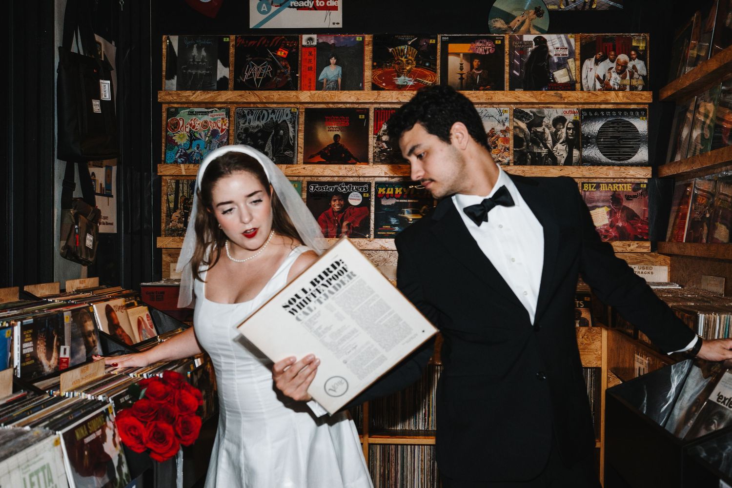 Couple in formal wedding attire browses through vinyl records at a music store.