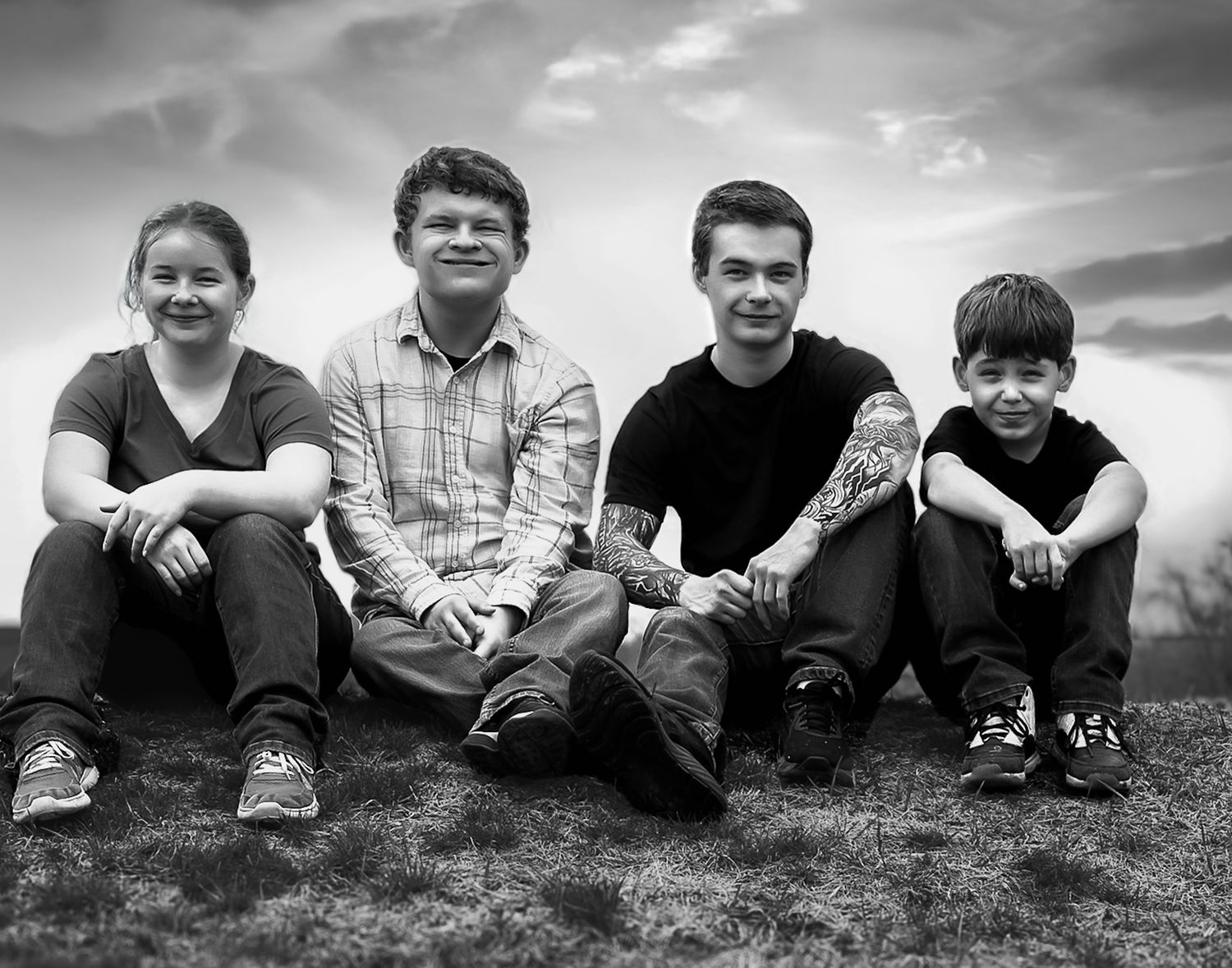 Black and white photo of people lying in grass against dramatic sky.