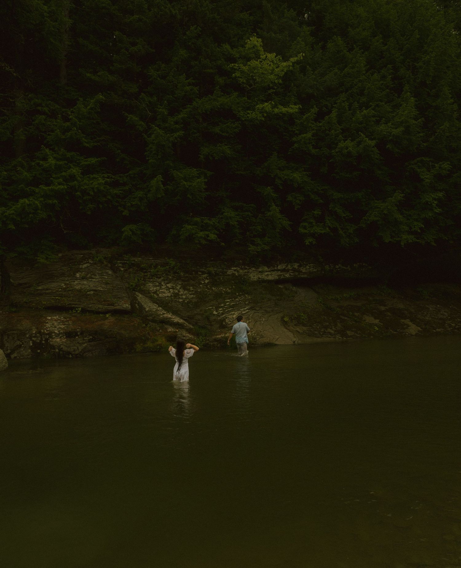 Dark wooded area with calm lake water reflecting dense forest surroundings. couple sexy romantic photoshoot in water