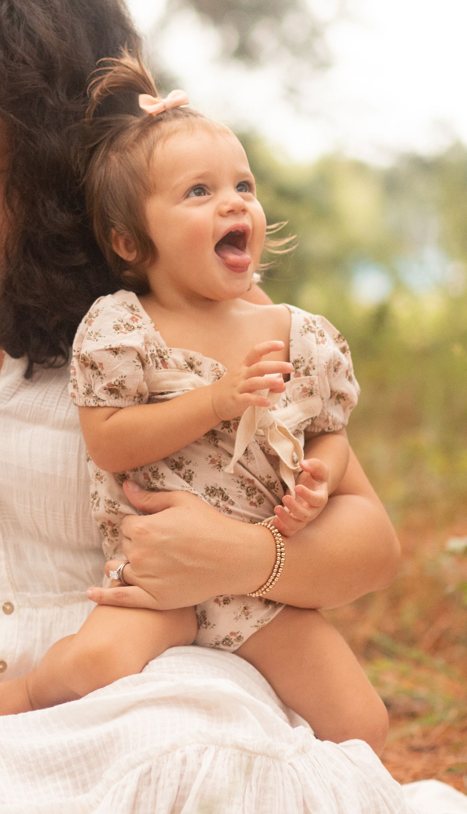 Young family of four enjoying outdoor lifestyle photos in a wooded field. Parents hold their toddler and baby girl while smiling.