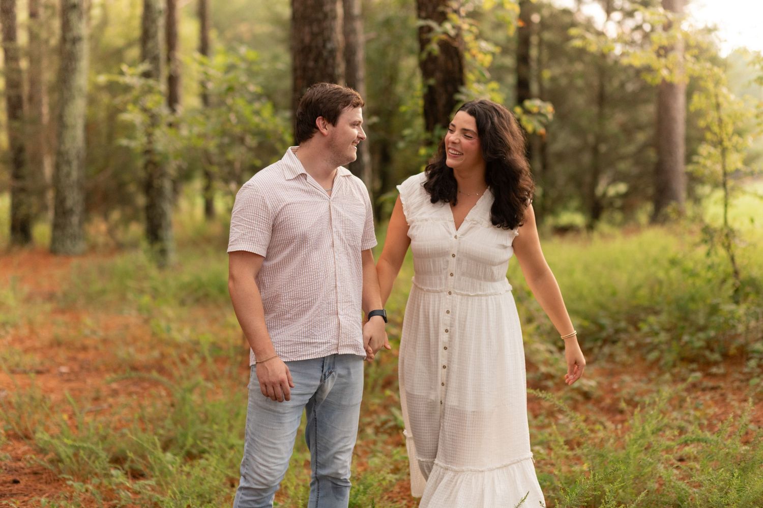 Young family of four enjoying outdoor lifestyle photos in a wooded field. Parents hold their toddler and baby girl while smiling.