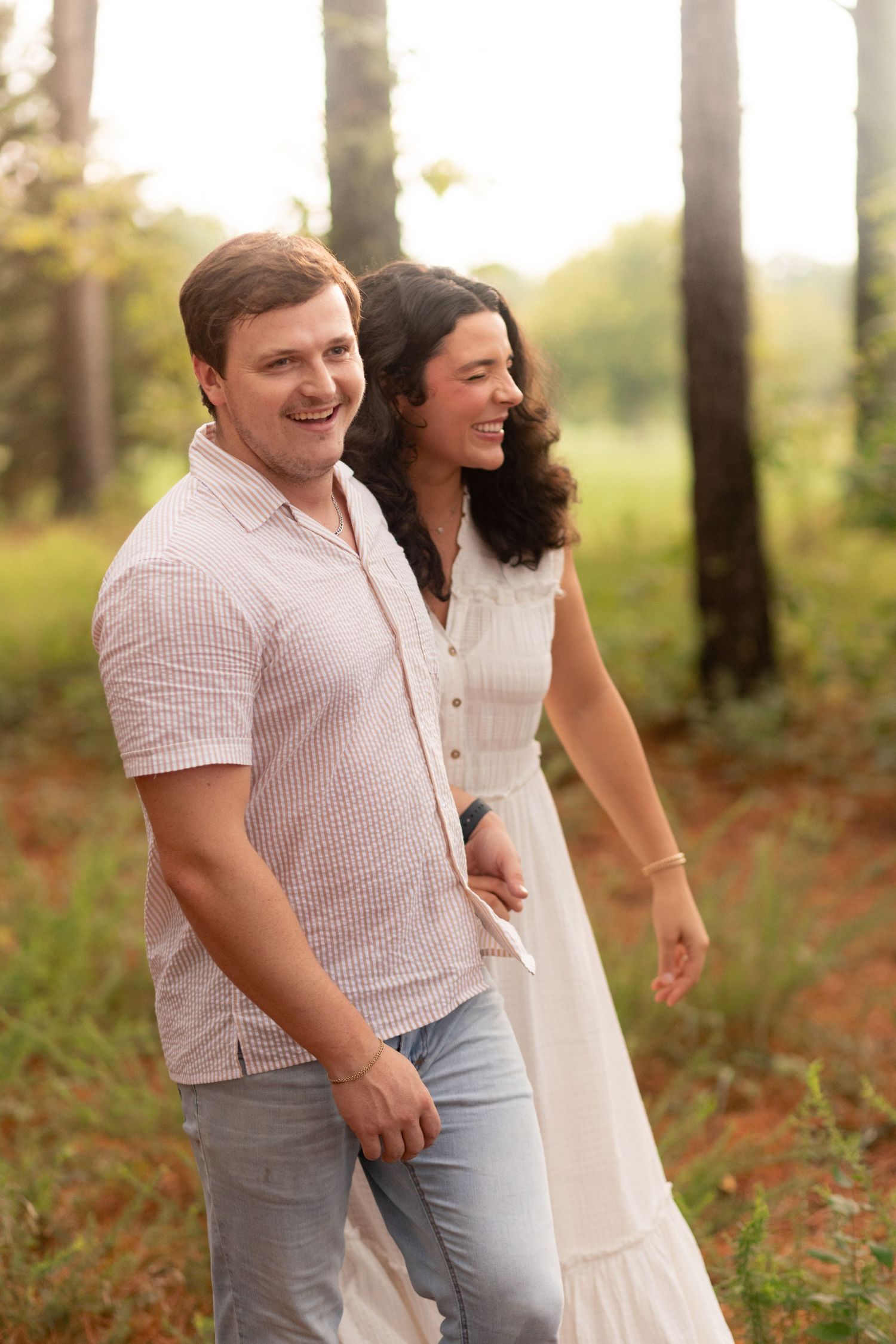 Young family of four enjoying outdoor lifestyle photos in a wooded field. Parents hold their toddler and baby girl while smiling.