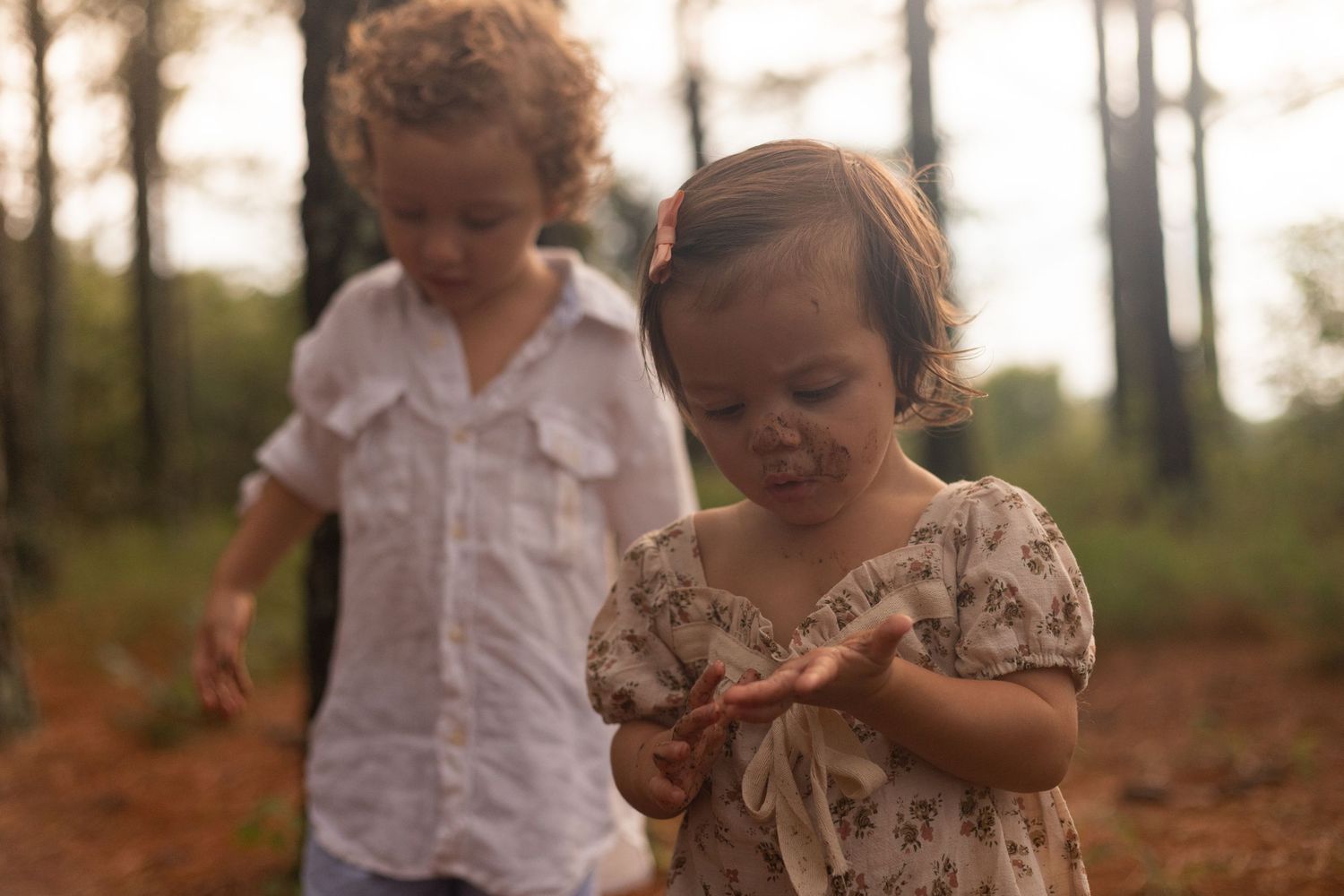 Young family of four enjoying outdoor lifestyle photos in a wooded field. Parents hold their toddler and baby girl while smiling.