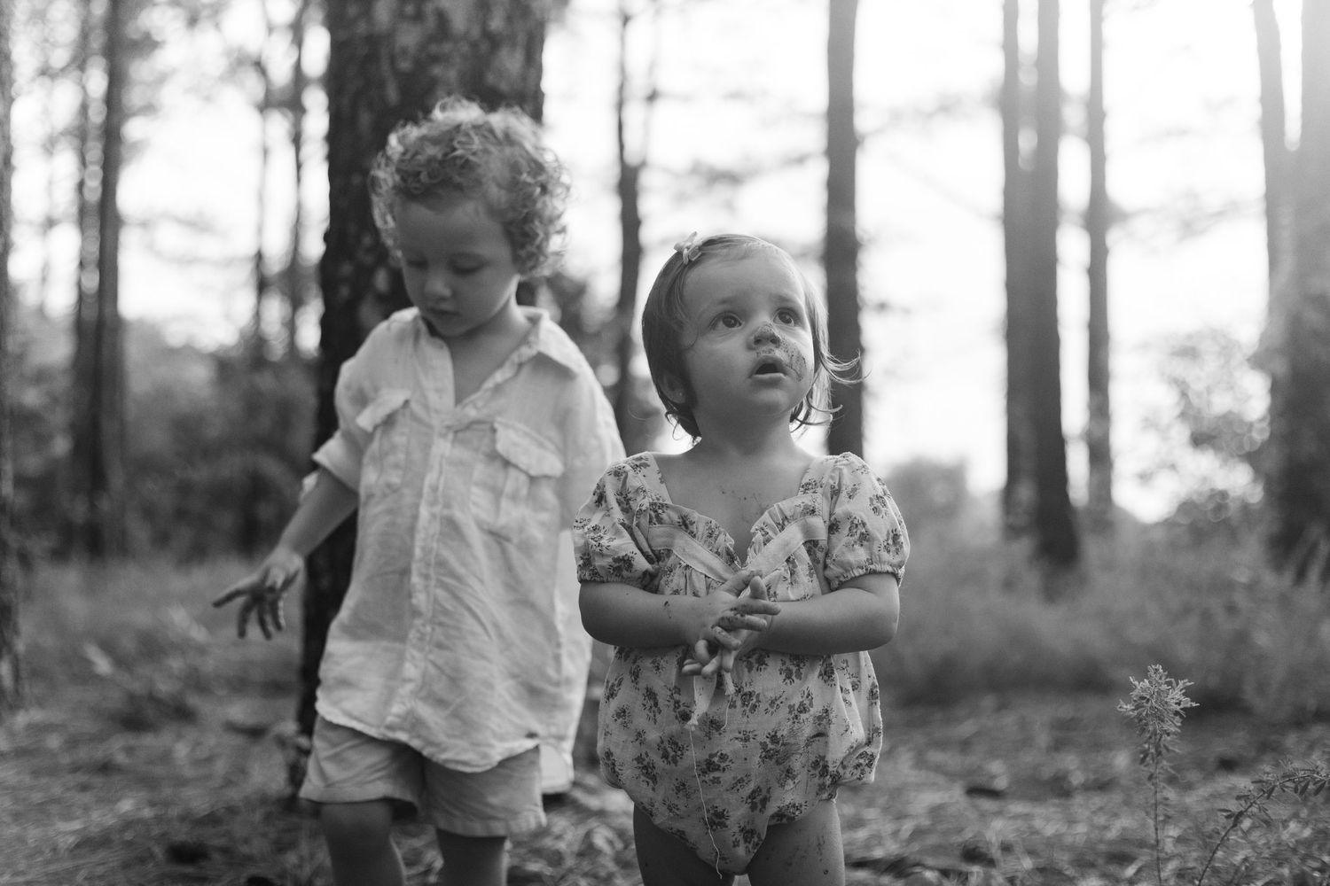 Young family of four enjoying outdoor lifestyle photos in a wooded field. Parents hold their toddler and baby girl while smiling.