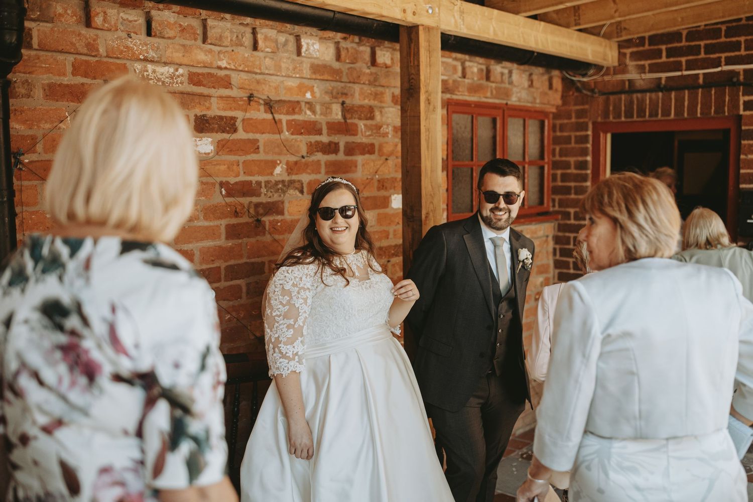 Bride and groom stand together on a brick porch during their wedding celebration with guests.
