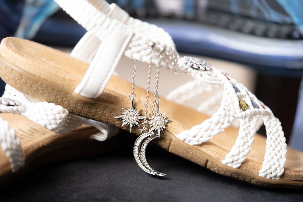 Wedding shoes in white and silver with delicate lace details arranged on a wooden surface with soft lighting.