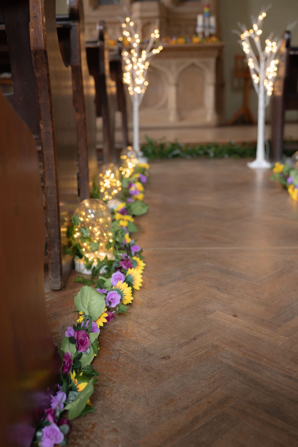 Floor-level view of colorful flower arrangements lining a church aisle with soft bokeh lighting in the background.