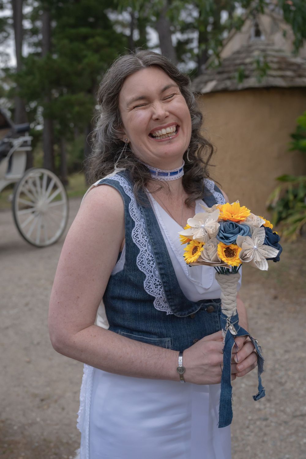 A person wearing a denim dress and white lace collar holds bright yellow and white flowers while laughing joyfully.